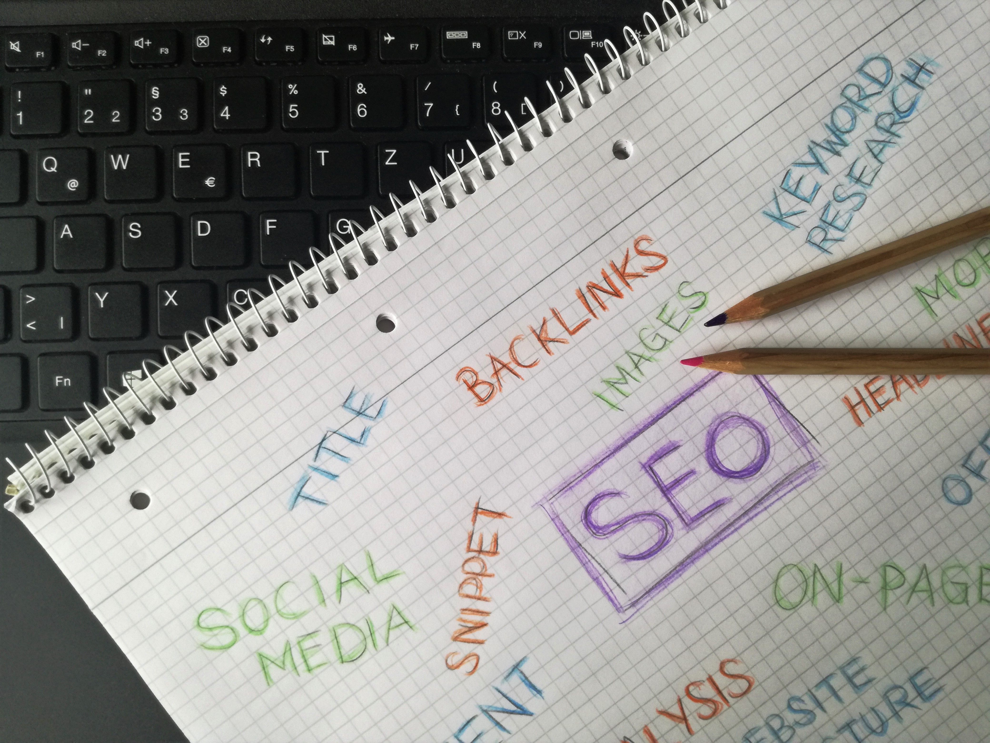 Notebook with SEO keywords and digital marketing terms written beside a laptop